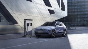 A new 2024 Hyunda Kona Electric plugged into a charging station in an urban landscape.