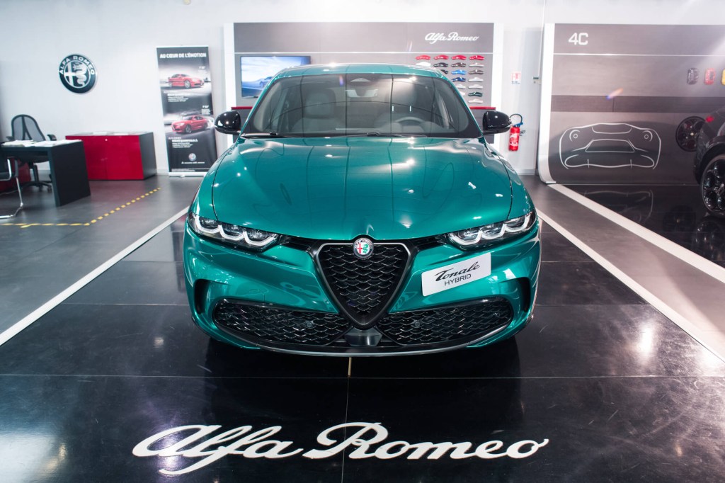 A green Alfa Romeo Tonale sits on a showroom floor with the Alfa Romeo logo in front. 