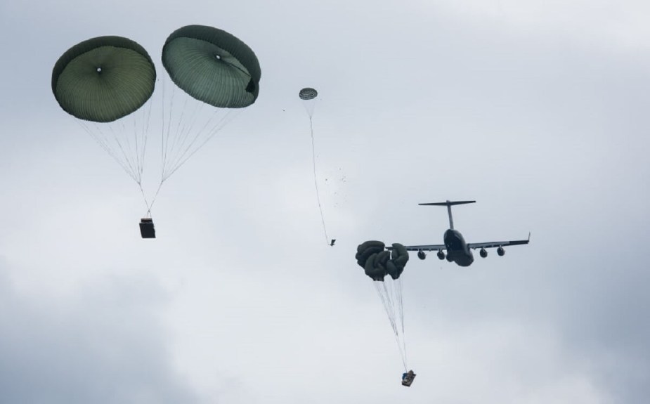 An airborne unit drops military vehicles and equipment like Humvees onto a battlefield. 