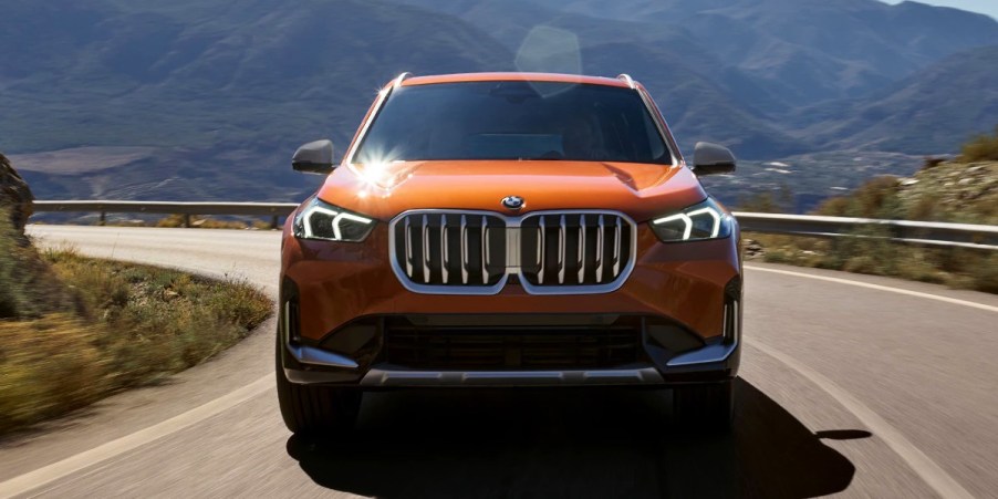 An orange BMW X1 subcompact SUV is driving on the road.