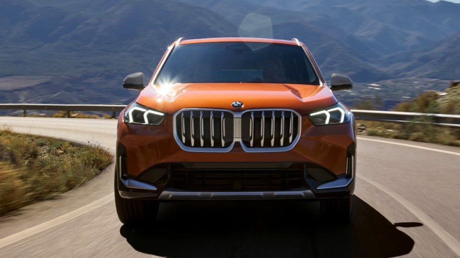 An orange BMW X1 subcompact SUV is driving on the road.