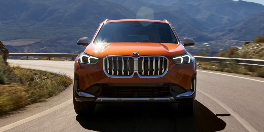 An orange 2023 BMW X1 subcompact SUV is driving on the road. 