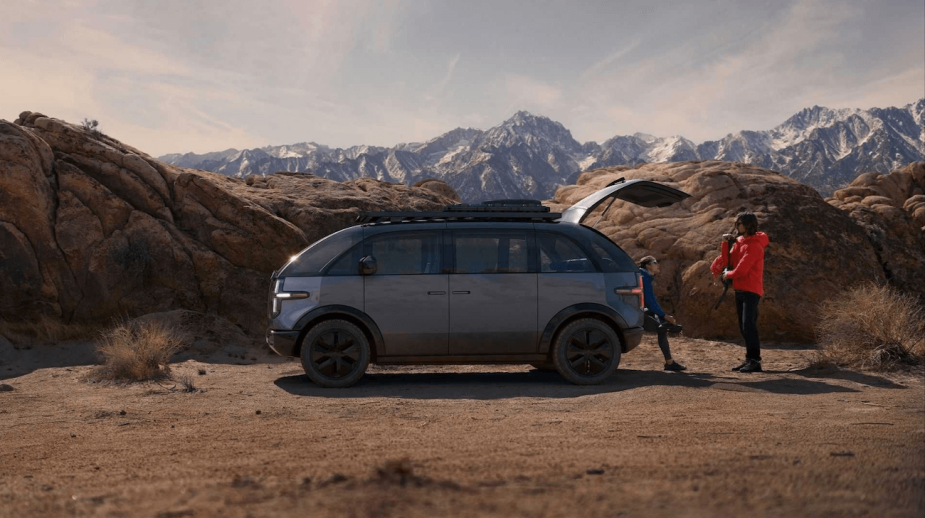 The 2023 Canoo Lifestyle Van is one of the coolest EVs qquickly approaching production. This one is parked inthe desert while people work on setting up camp.