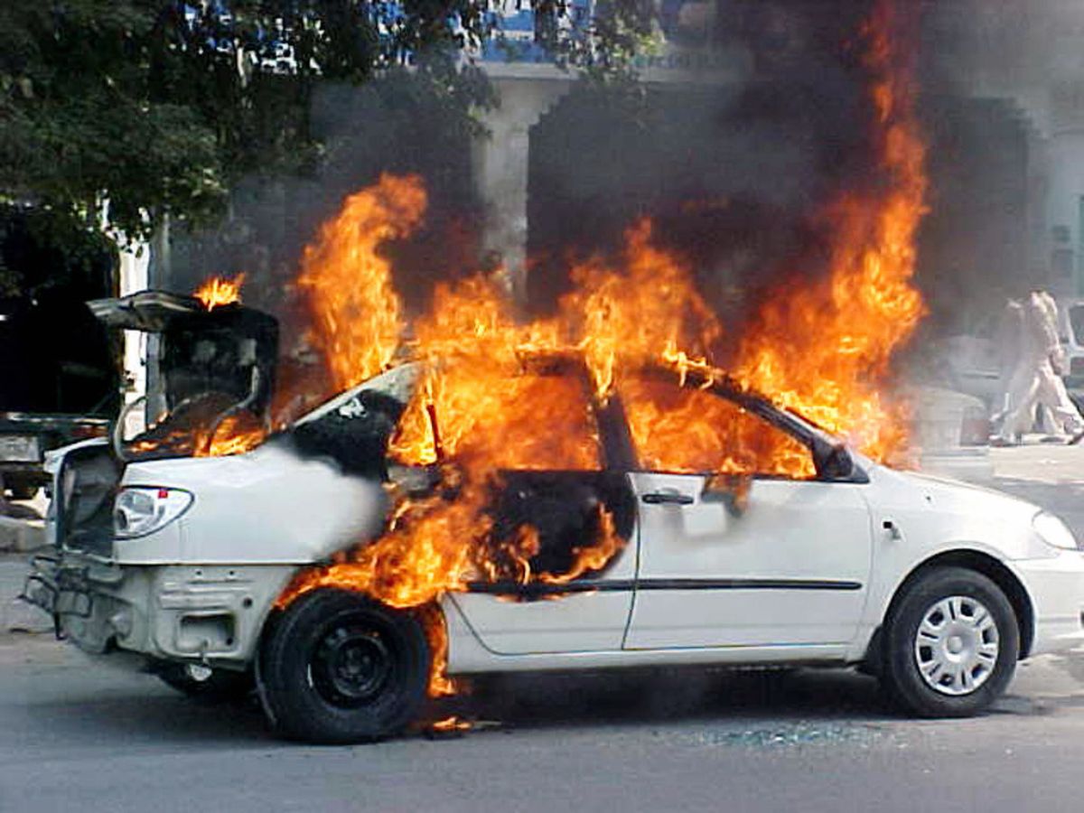 A small white car on fire, engulfed in flames.