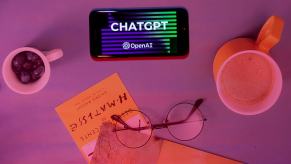 ChatGPT from OpenAI on a smartphone next to coffee, books, and glasses, on a table