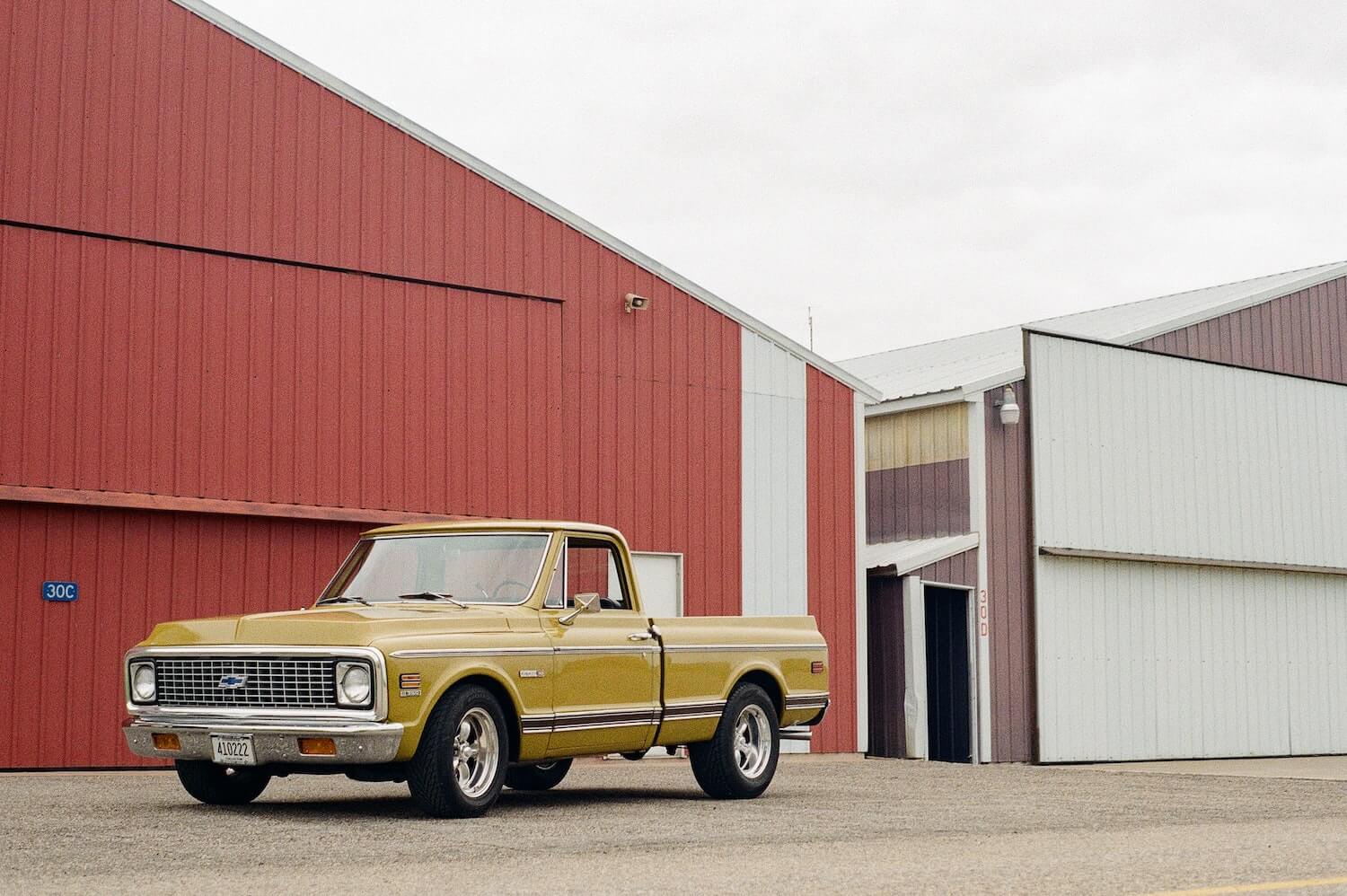 A golden colored Chevrolet 1500 square body generation pickup truck parked in front of a red barn.