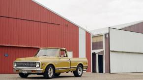 A golden colored Chevrolet 1500 square body generation pickup truck parked in front of a red barn.
