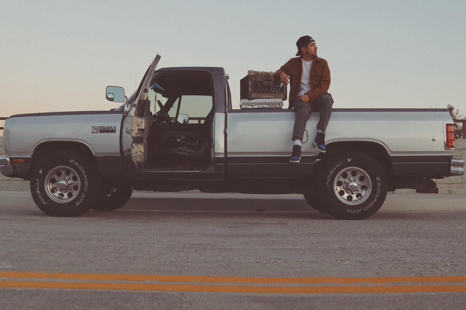 A man sits on the bed of his regular cab Dodge Ram pickup truck.