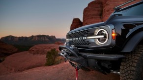 A black Ford Bronco sits amid red rocks at sunset.