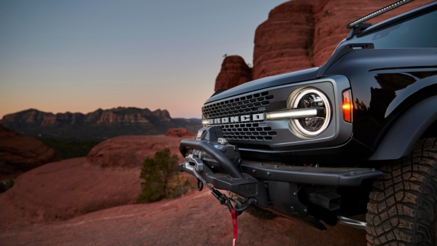 A black Ford Bronco sits amid red rocks at sunset.