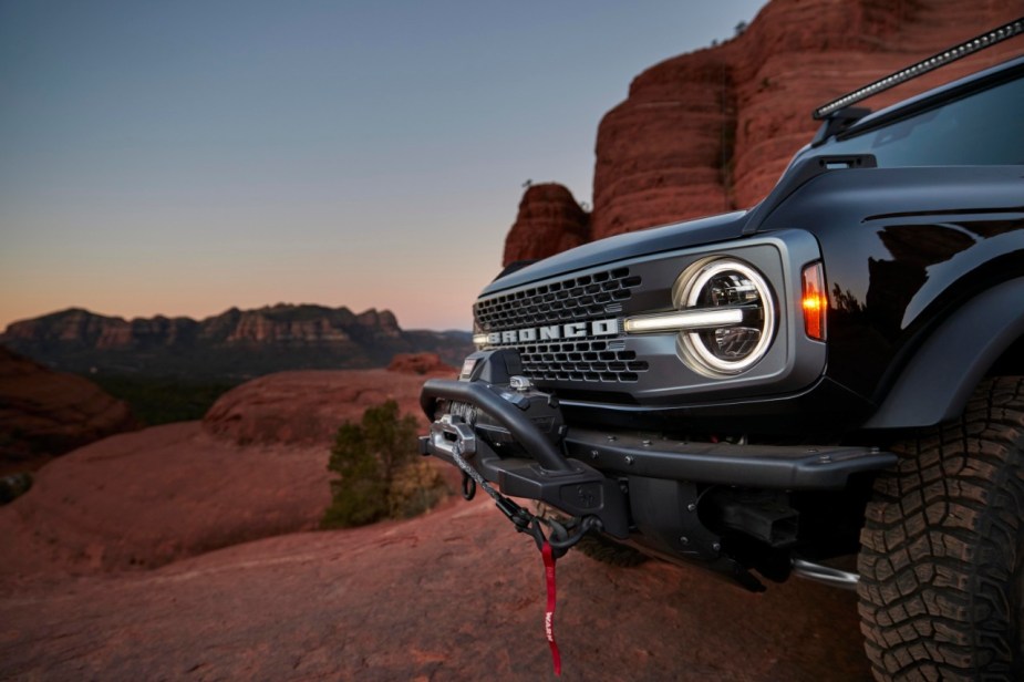 A black Ford Bronco sits amid red rocks at sunset.
