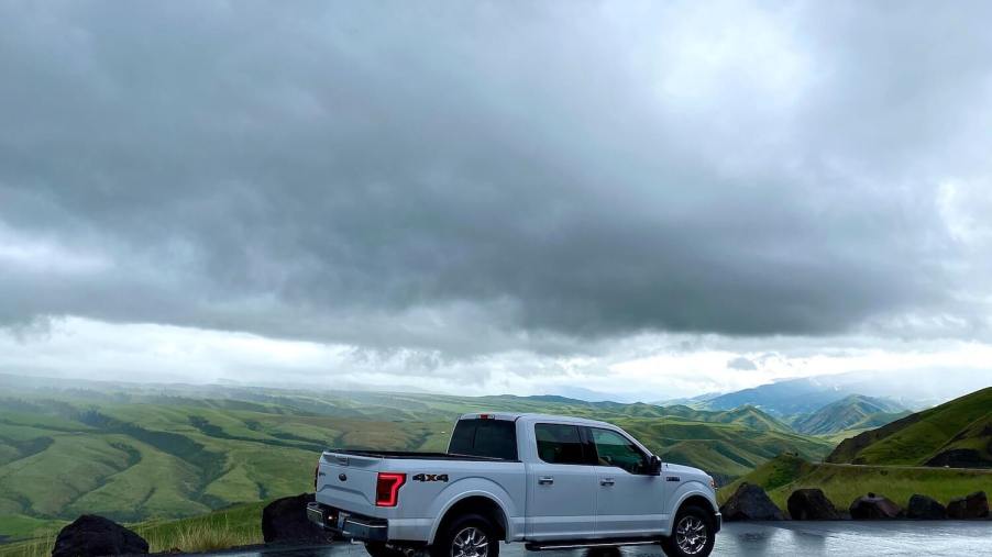 A white F-150 parked on a mountain road, a mountain range and dark clouds visible in the background.