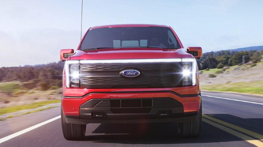 A red Ford F-150 Lightning electric pickup truck is driving on the road.