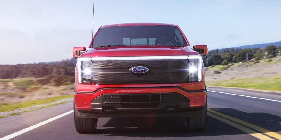 A red 2023 Ford F-150 Lightning electric pickup truck is driving on the road. 