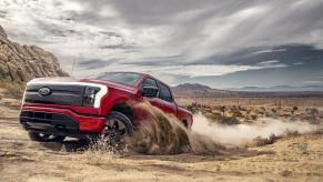 A red 2023 Ford F-150 Lightning drives through dirt as an electric truck.