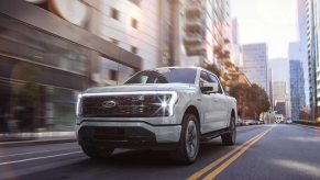The Ford F-150 Lightning is driving through a city. Electric pickup trucks have some distinct advantages over ICE trucks.