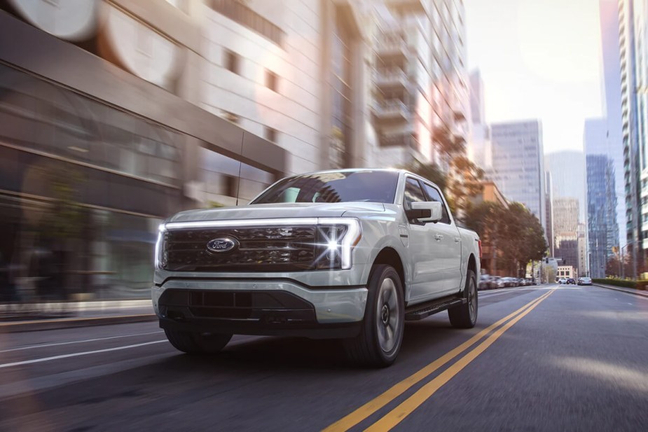 The Ford F-150 Lightning is driving through a city. Electric pickup trucks have some distinct advantages over ICE trucks.