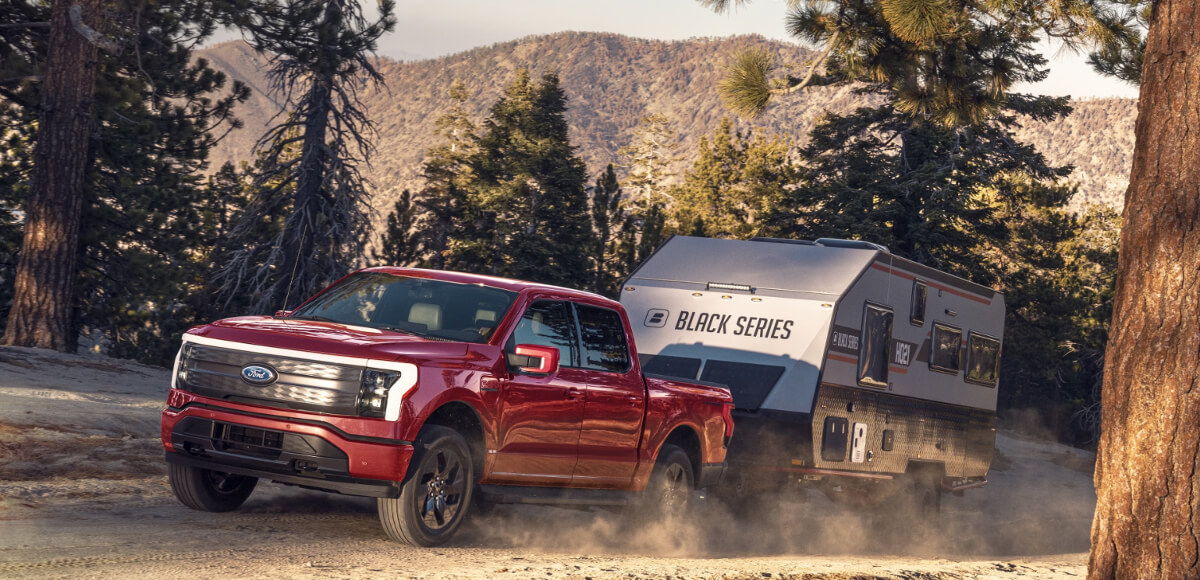 A 2023 Ford F-150 Lightning is towing a trailer behind it as an electric truck.