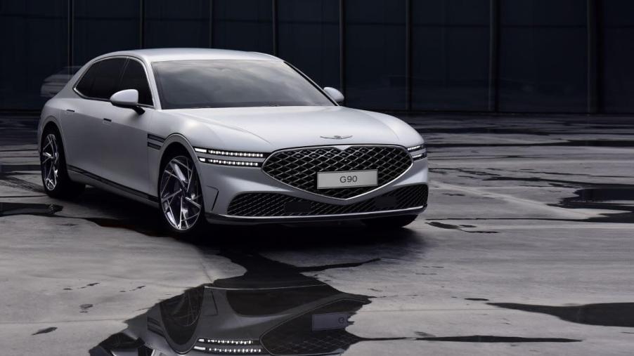 A silver-gray Genesis G90 luxury full-size sedan model parked on an asphalt floor splattered with water puddles