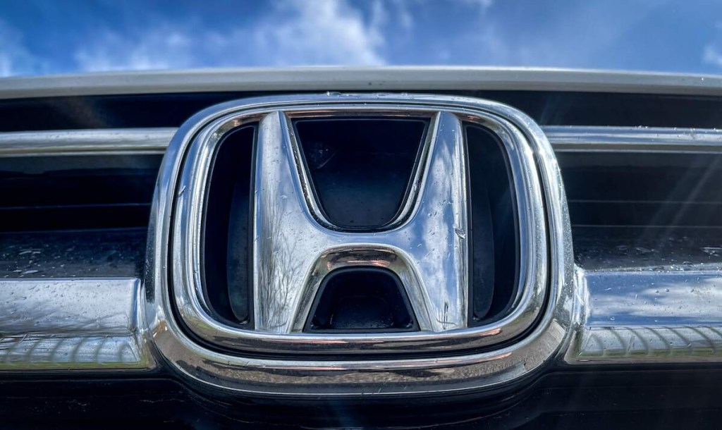 A silver Honda logo on a grille with a blue sky in the background. 