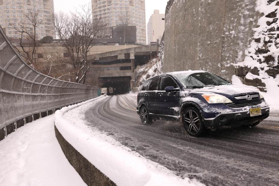 A Honda CR-V climbs a hill amid snowy conditions in an urban setting. 