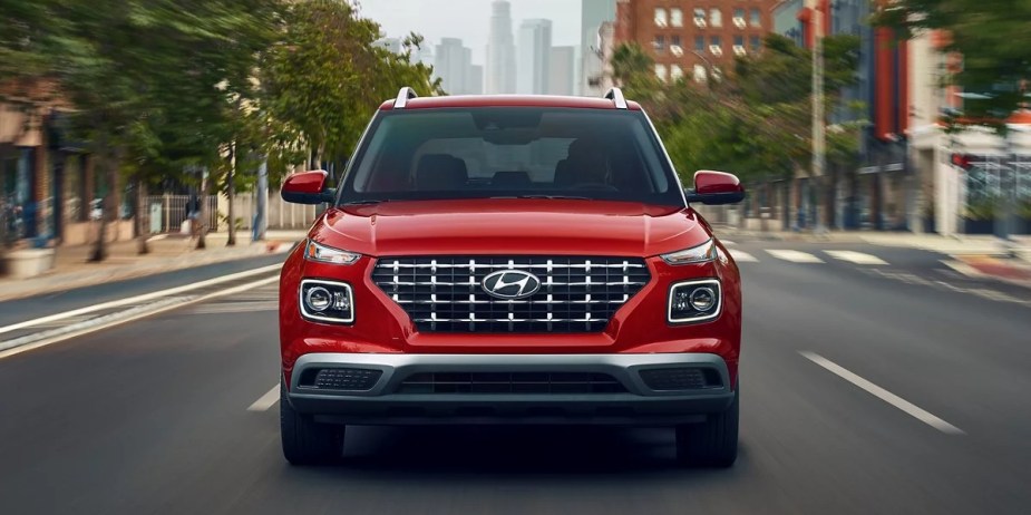 A red Hyundai Venue subcompact SUV is driving down the road. 