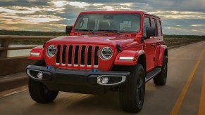 A red 2023 Jeep Wrangler small SUV is driving on the road.