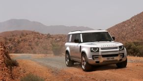 A white 2023 Land Rover Defender 130 drives near some mountains
