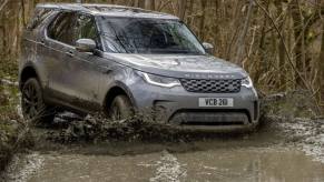A gray Land Rover Discovery full-size luxury SUV model driving off-road through rivers of mud in a forest