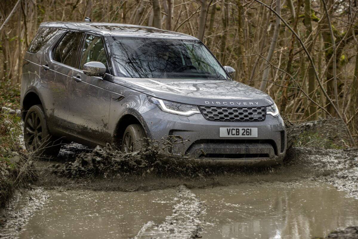 A gray Land Rover Discovery full-size luxury SUV model driving off-road through rivers of mud in a forest