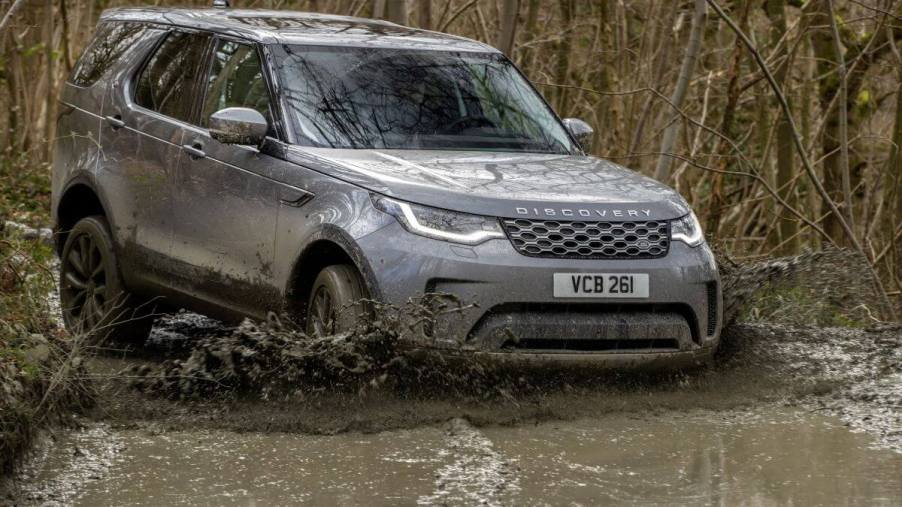 A gray Land Rover Discovery full-size luxury SUV model driving off-road through rivers of mud in a forest