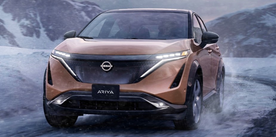 A copper 2023 Nissan Ariya small electric SUV is driving off-road in the snow. 