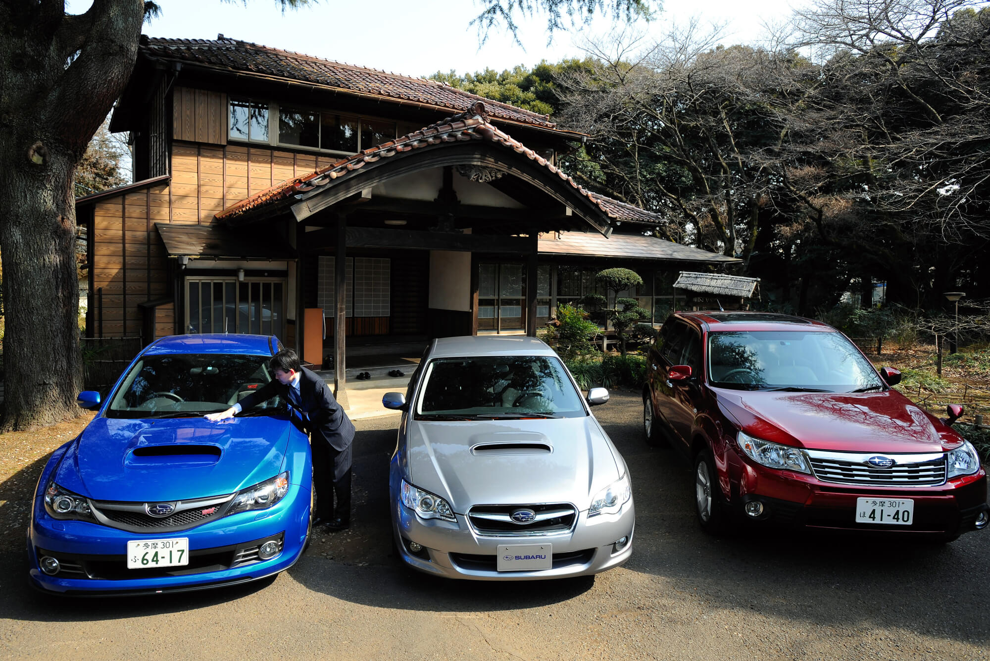 A group of 2000s Subaru models parked in front of a house.