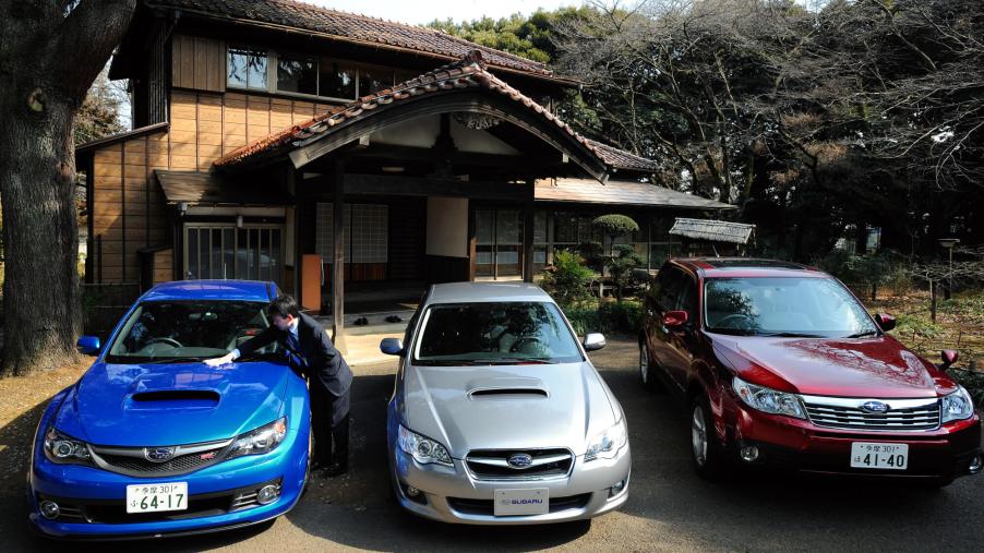 A group of 2000s Subaru models parked in front of a house.