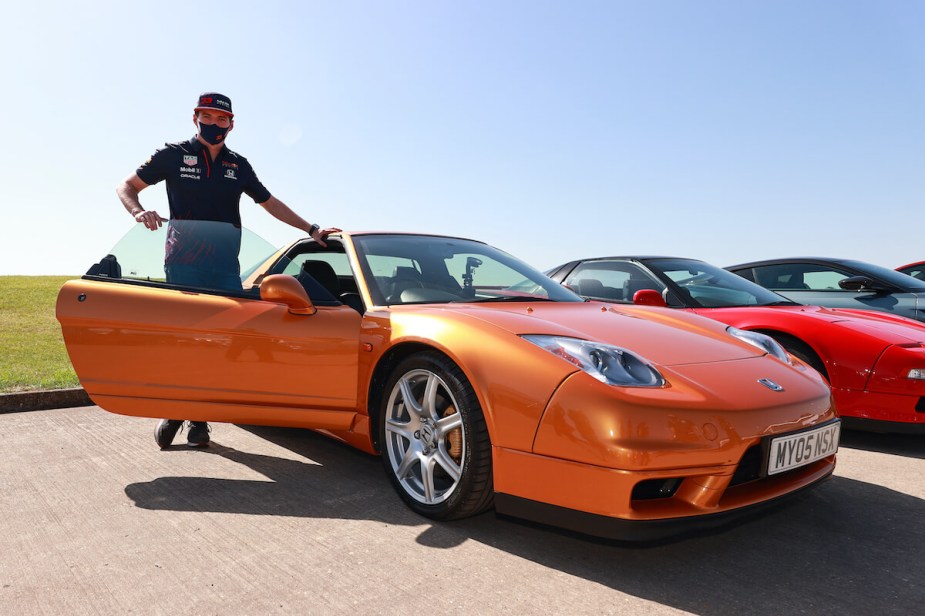 A racecar driver standing next to an orange Acura NSX.