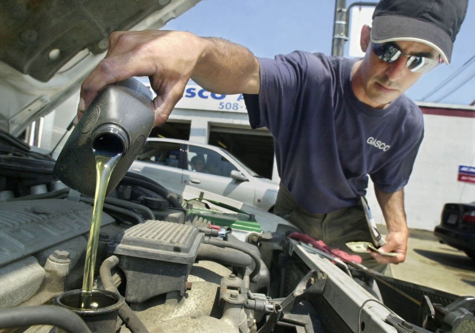 An automotive technician working at a service center pours oil into a motor with the spout at the top of the jug.