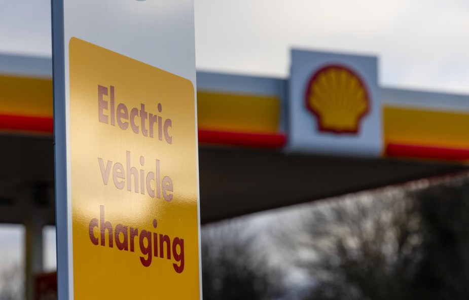 A yellow and red sign reads "EV vehicle charging" at a shell convenience stop.