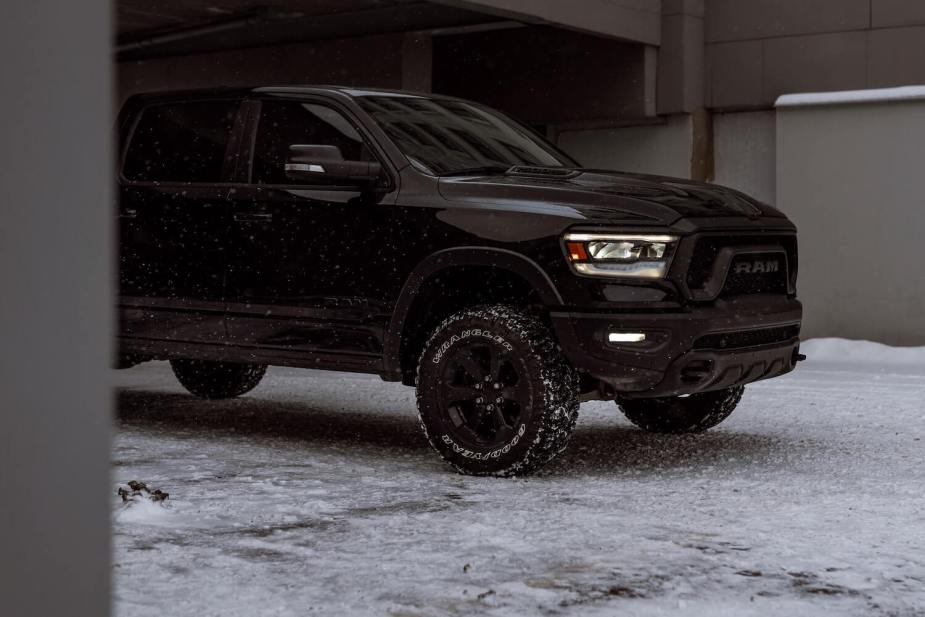 A black Ram 1500 pickup truck parked beneath a roof, on snowy pavement.