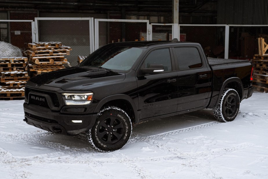 A black Ram 1500 pickup truck parked in front of a stack of pallets by a loading bay, in the snow.