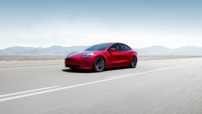 A red 2023 Tesla Model 3 blasts down an open road at speed, buoyed by its top safety scores.
