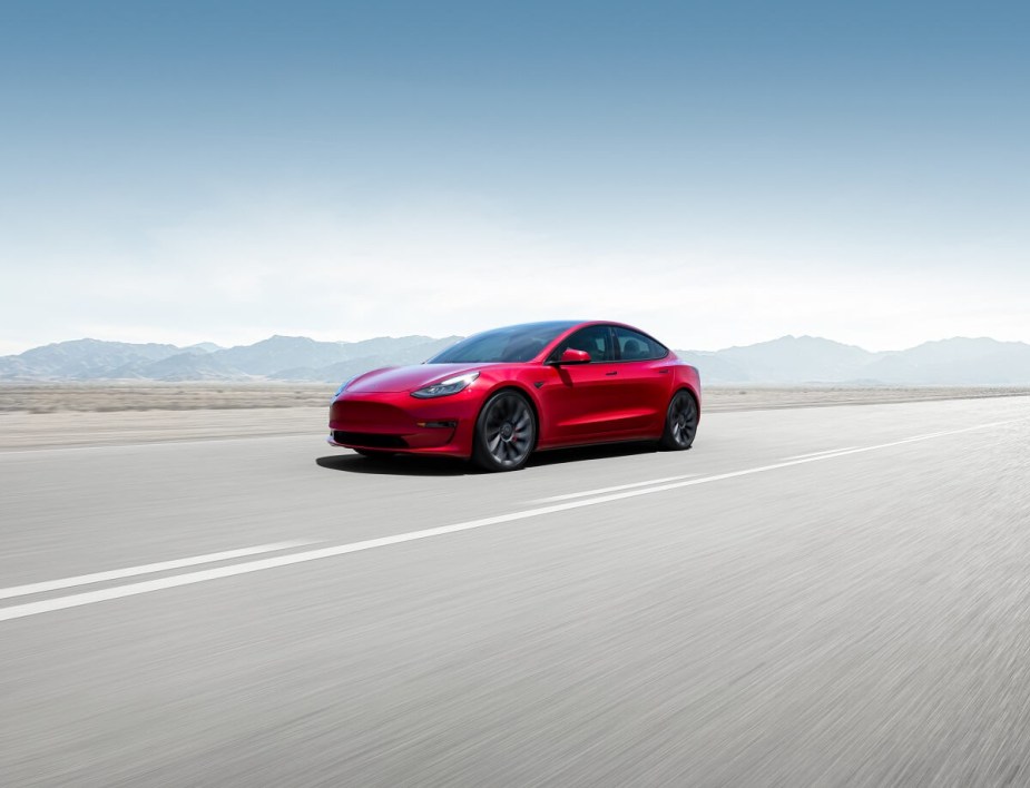 A red 2023 Tesla Model 3 blasts down an open road at speed, buoyed by its top safety scores. 