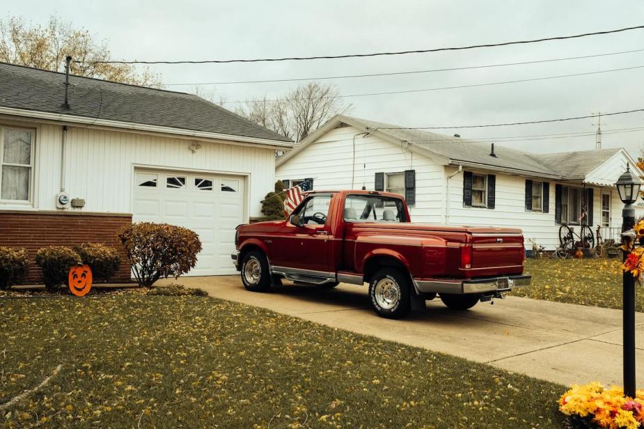 Red Ford F-150 pickup truck parked in front of a white one-story home on a suburban street.