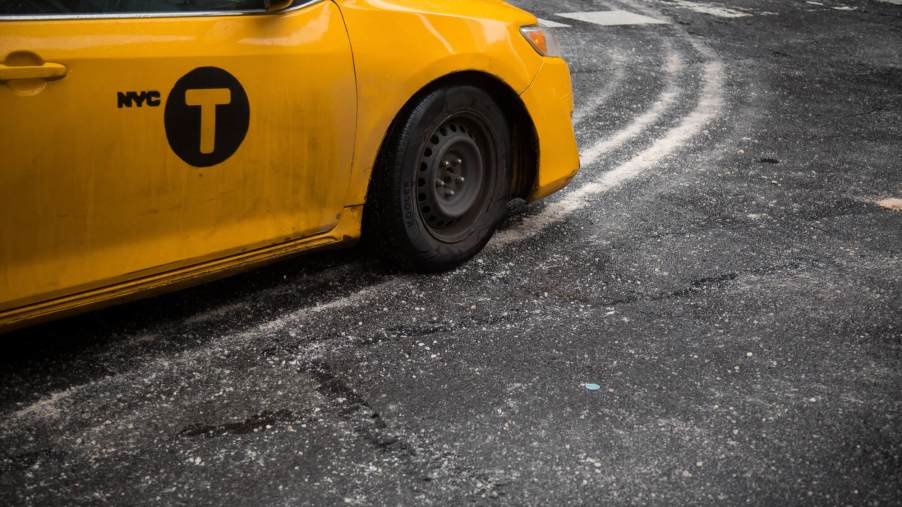 A yellow taxi drives on a street covered in road salt.