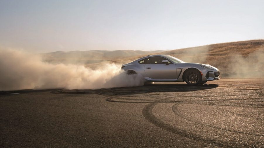 A 2023 Subaru BRZ sports car shows off its silver paintwork as it safely drifts on the sandy tarmac.