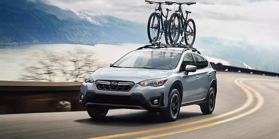 A blue 2023 Subaru Crosstrek subcompact SUV is driving on the road with two bikes on top of it. 