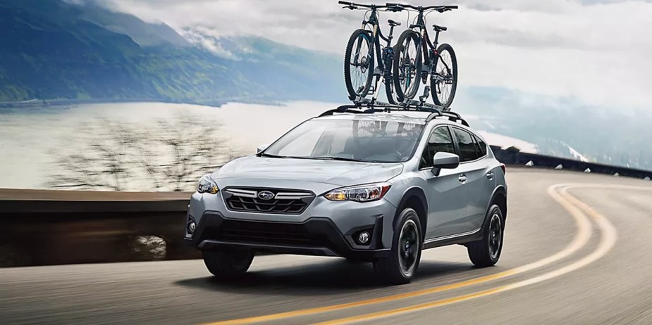 A blue 2023 Subaru Crosstrek subcompact SUV is driving on the road with two bikes on top of it.