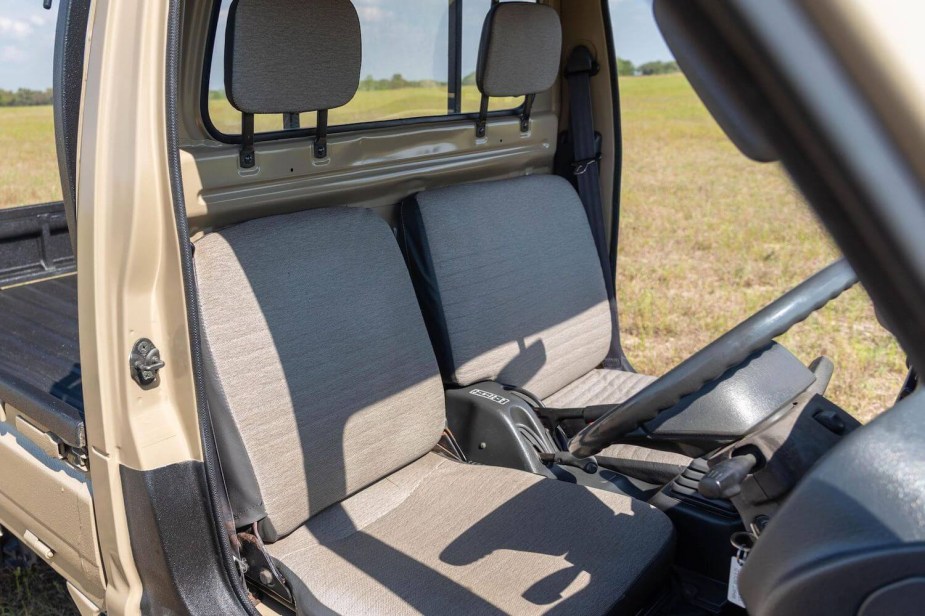 Interior of a Suzuki Carry "Kei-Class" mini truck, its doors open and a field visible in the background.