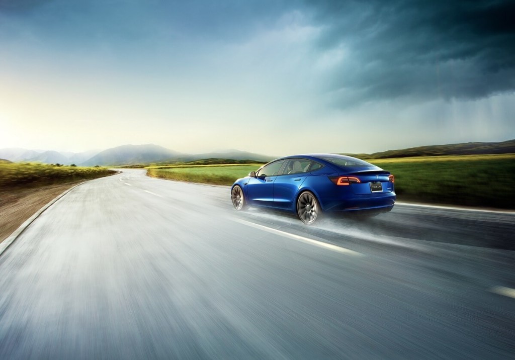 A blue Tesla Model 3 Performance blasts down a wet road. 