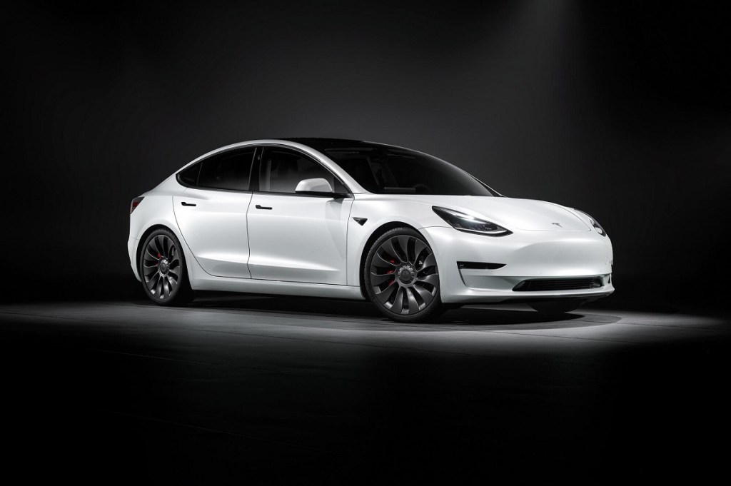 A white 2023 Tesla Model 3 poses in a dark studio. 