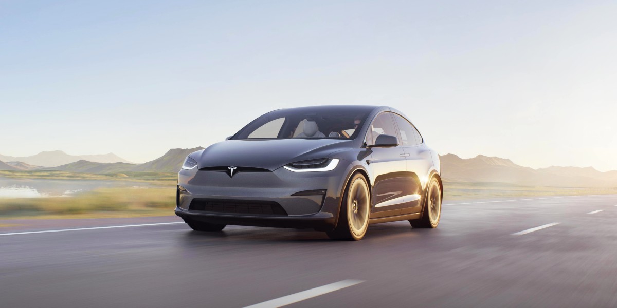 A gray 2023 Tesla Model X midsize SUV is driving on the road.